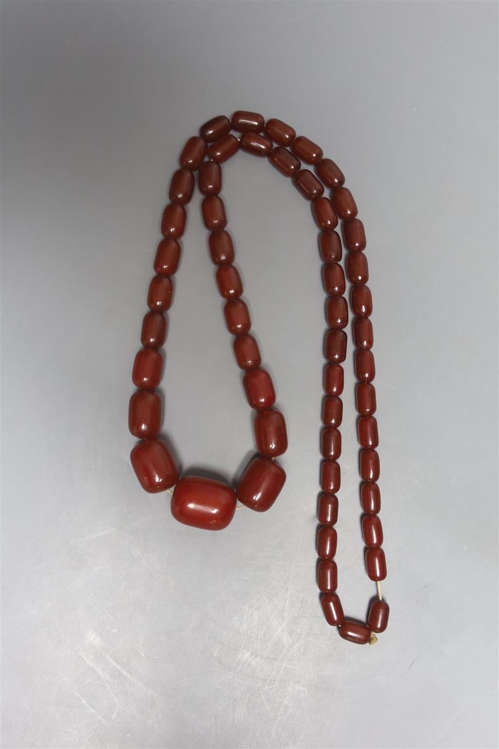 A single strand graduated simulated cherry amber barrel shaped bead necklace, 90cm, gross 87 grams.